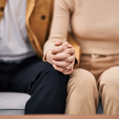 Mand and woman couple sitting on sofa with hands together at home